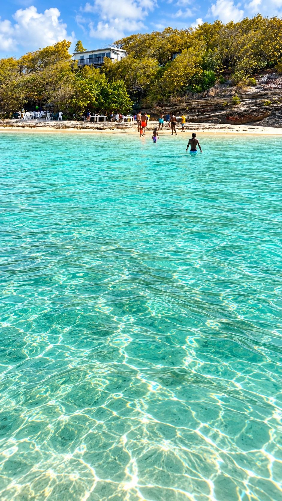 Baigneurs marchant dans l'eau turquoise peu profonde devant un îlet du François